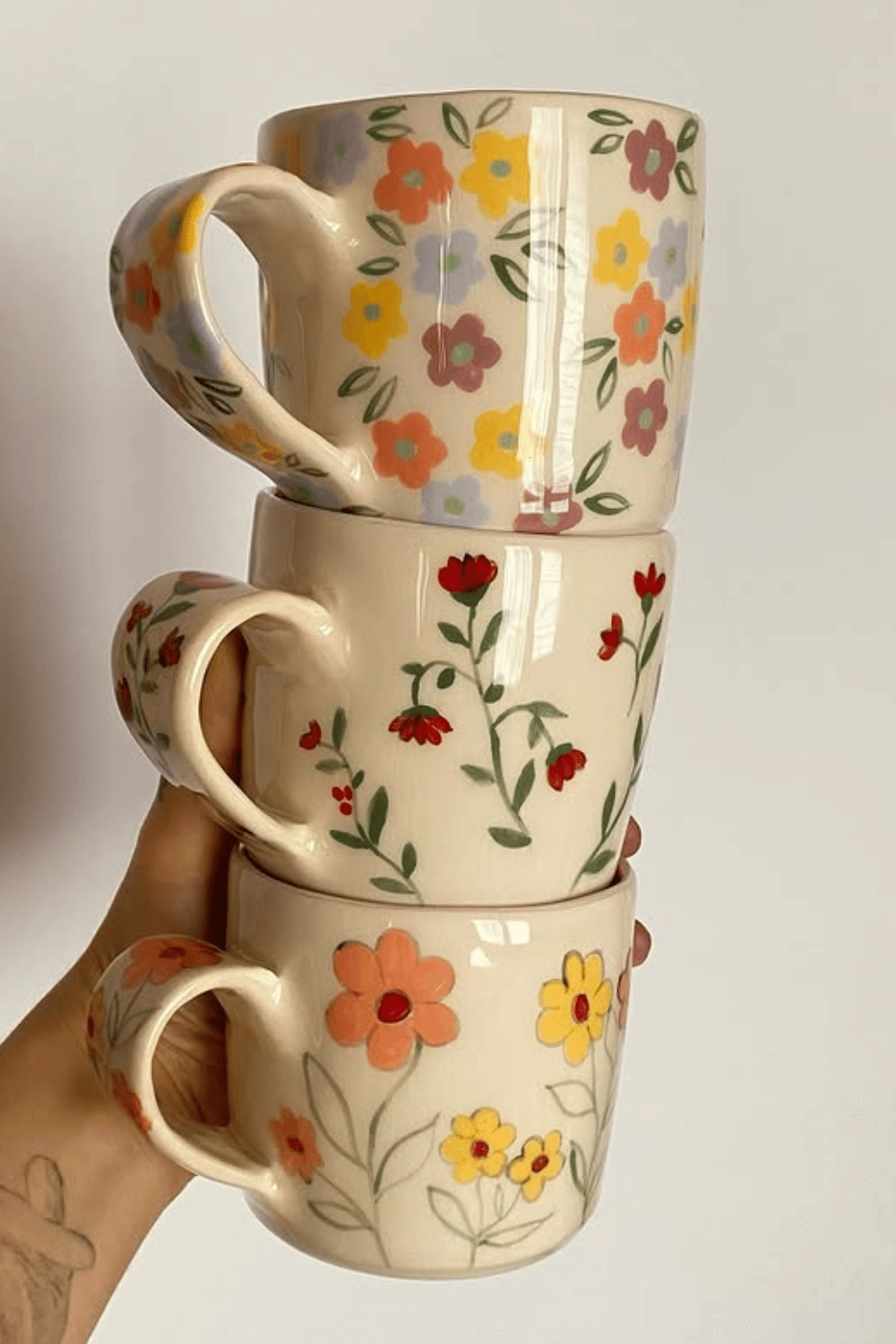 Stack of hand-painted floral ceramic mugs in cheerful colors make one of the most perfect DIY Mother's Day Gifts From Adults