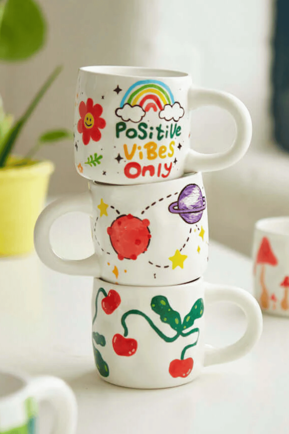 Kid-decorated mugs with rainbows, planets, and cherries