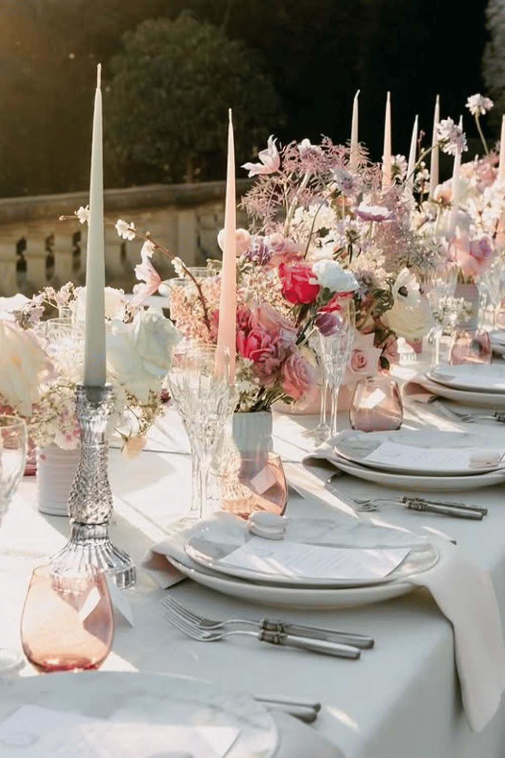 Romantic pastel wedding table with tall taper candles and soft floral arrangements