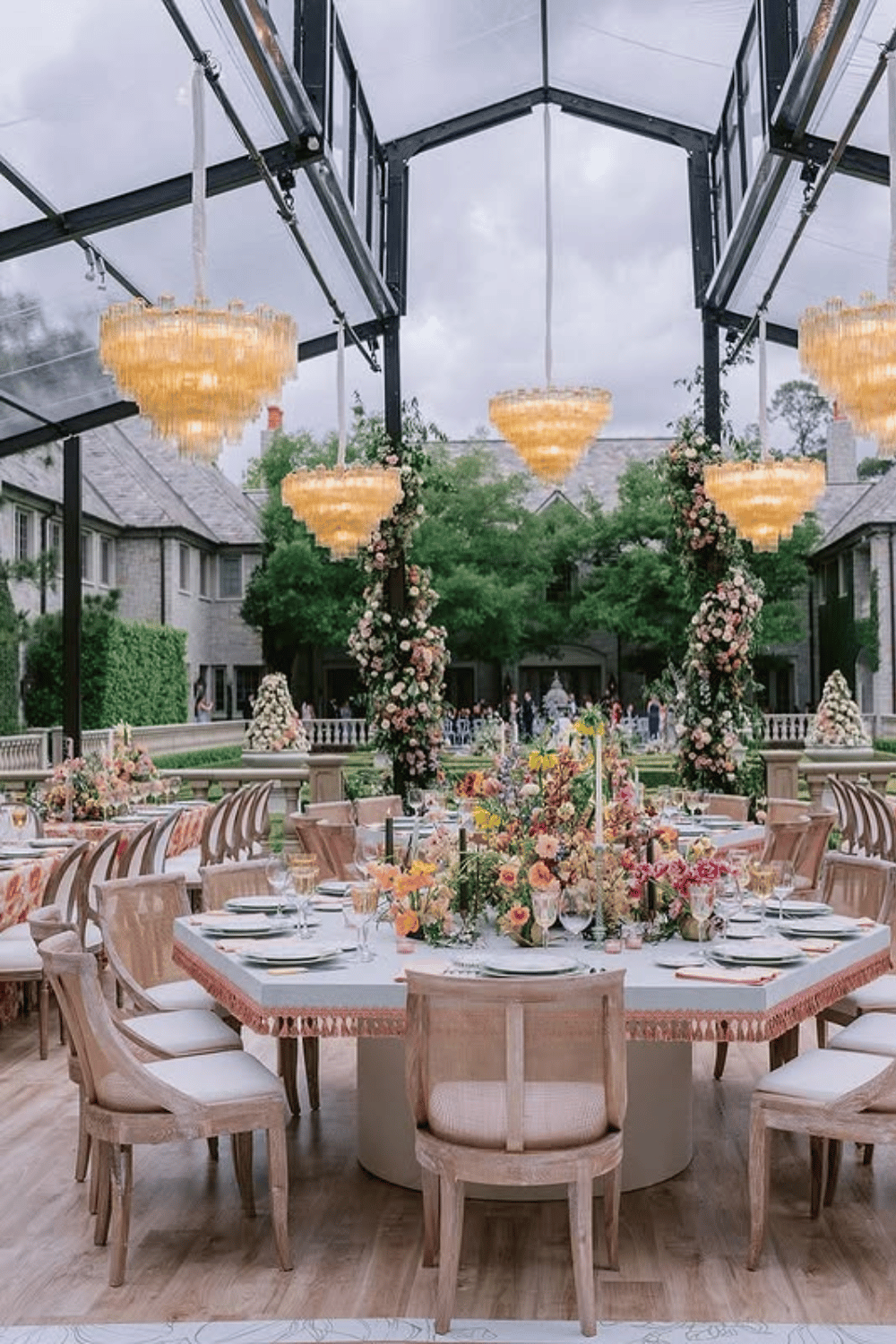 Lavish tented wedding reception with chandeliers and overflowing flower arrangements