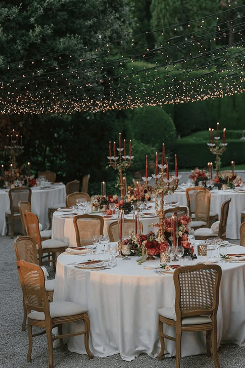 Romantic evening wedding table with red florals, gold candelabras, and white linens