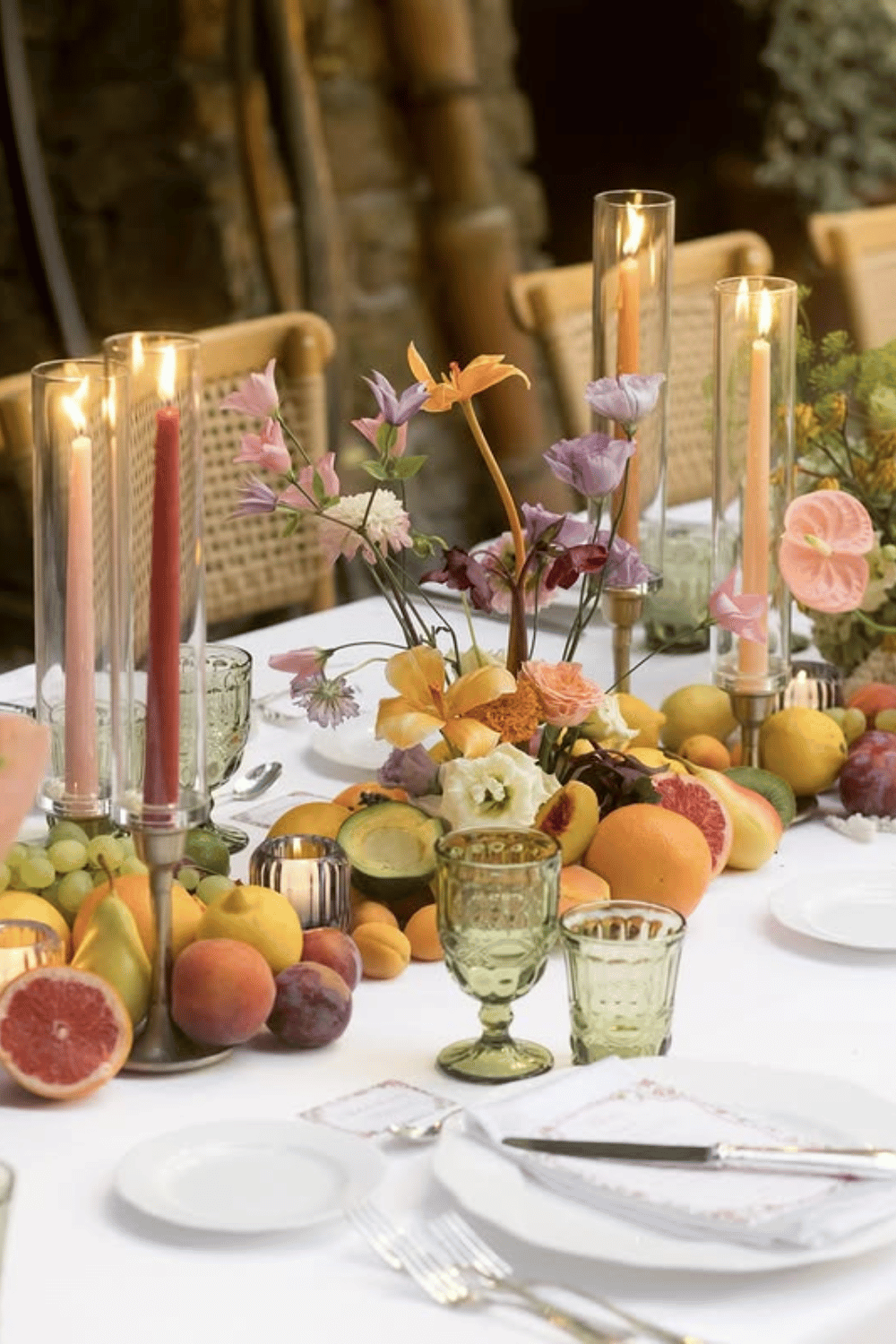 Vibrant wedding centerpiece with fresh fruit, flowers, and colorful taper candles