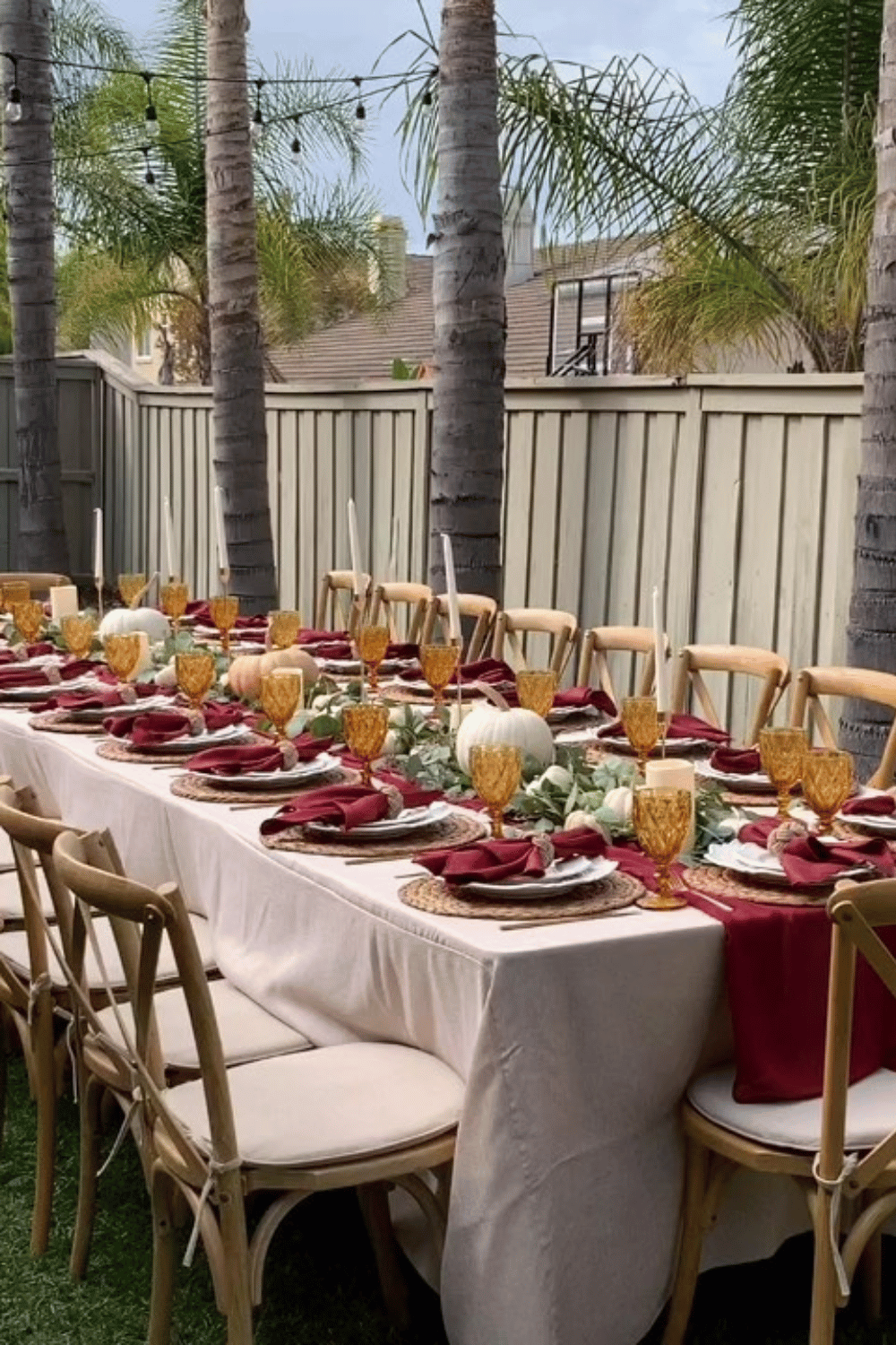 Rustic outdoor table setup with burgundy napkins, amber glasses, and pumpkins
