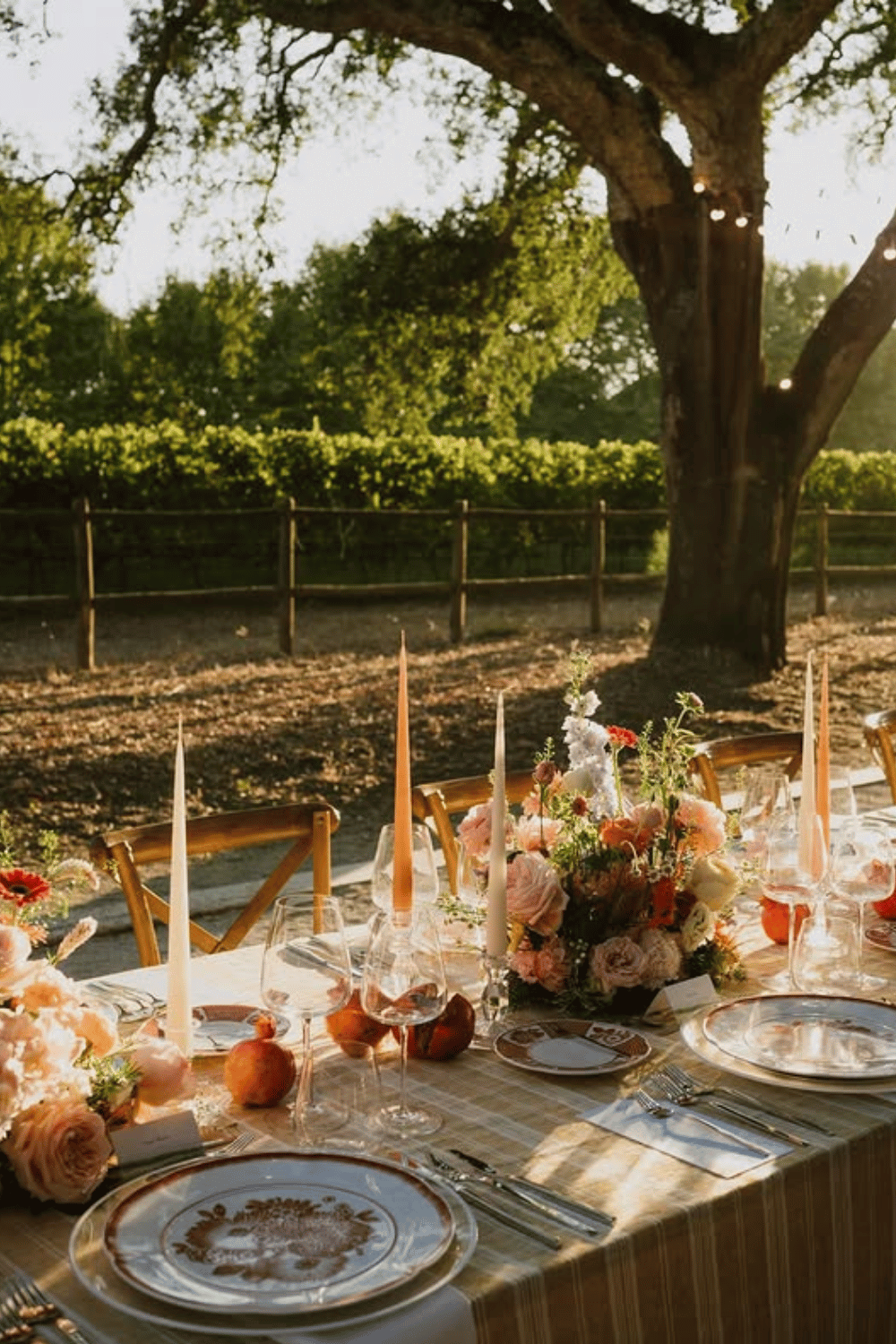 Outdoor wedding table with peach and rust tones under tree canopy at sunset