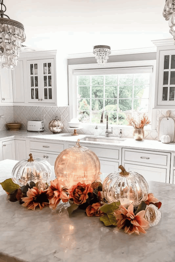 Fall kitchen island decorated with three glowing glass pumpkins and a garland of blush and rust florals