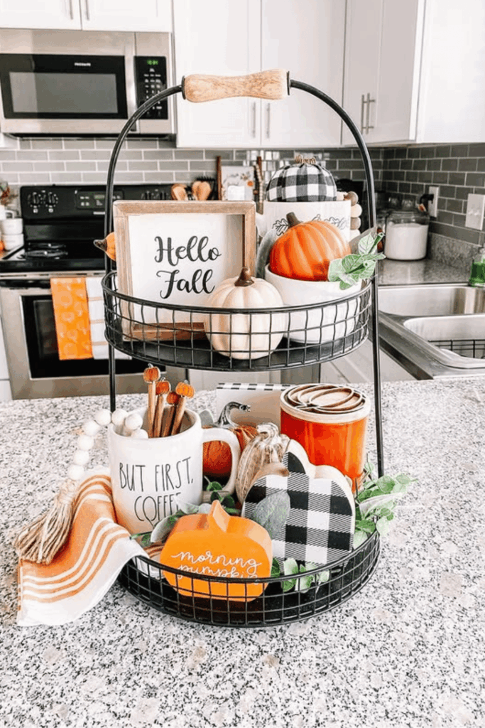 Two-tiered black tray decorated with fall mugs, mini pumpkins, and a Hello Fall sign on a kitchen counter