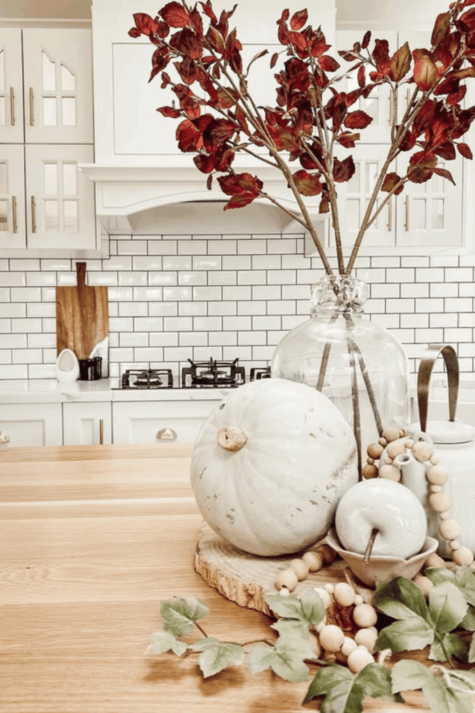 Neutral fall kitchen island with white pumpkin, wood bead garland, and vase of red autumn leaves