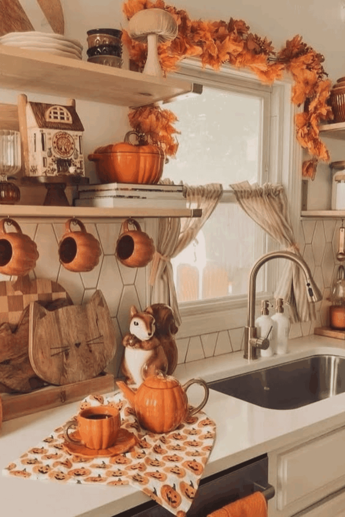 Warm fall kitchen decor with pumpkin mugs, orange garland, and squirrel-shaped teapot by window