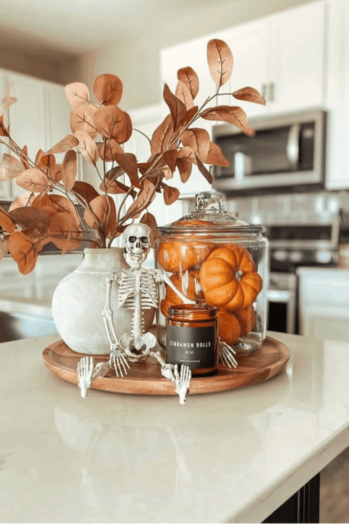 Fall kitchen centerpiece with skeleton figurine, jar of mini pumpkins, cinnamon candle, and vase of branches