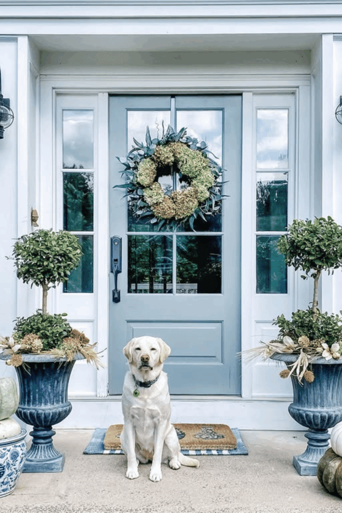 Porch with evergreens, neutral pumpkins, and soft-toned fall wreath