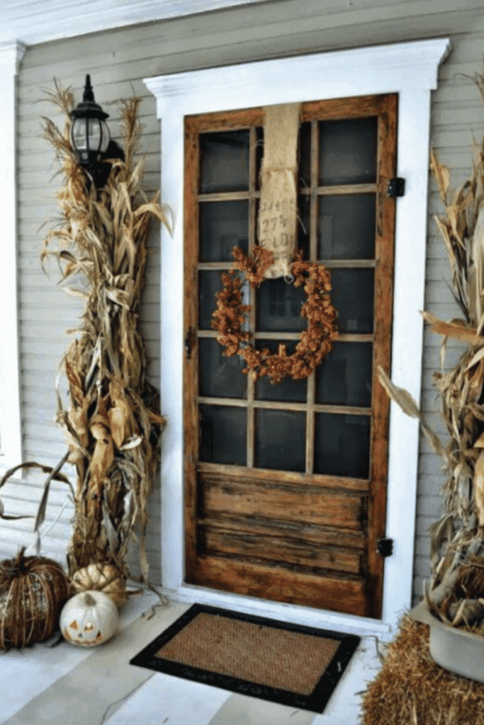 Front porch decorated with corn stalks, pumpkins, hay bales, and autumn wreath