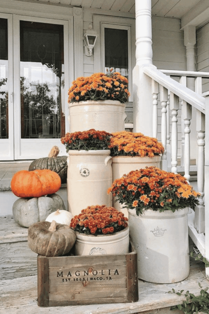 Vintage containers filled with colorful fall mums and pumpkins on a porch