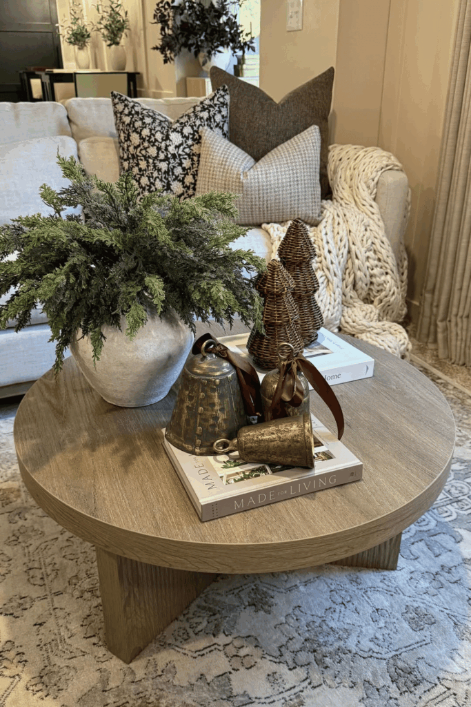 Cozy coffee table styled with greenery, brass bells, and neutral pillows