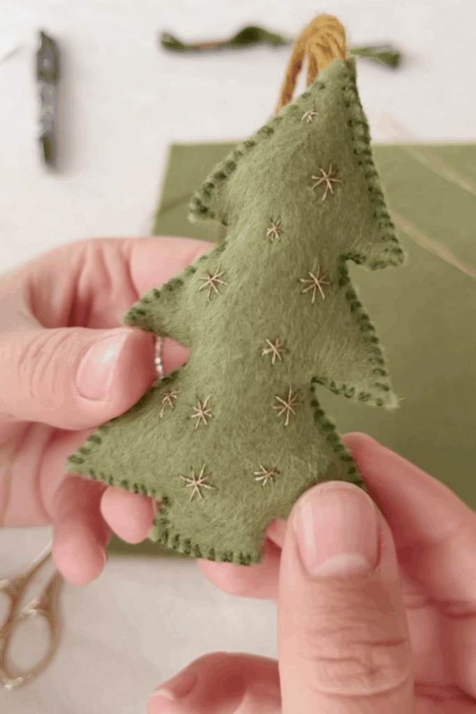 Green felt Christmas tree ornament with starburst embroidery held in hands