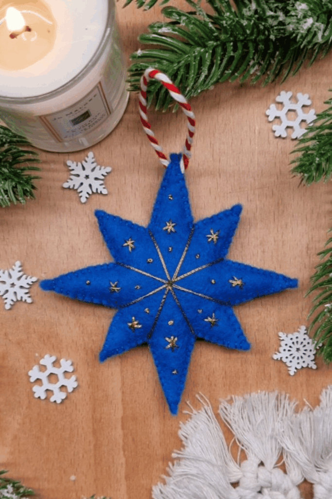 Bright blue felt star ornament with gold stitching surrounded by winter decorations